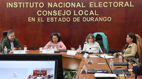 cuatro personas sentadas en una mesa en el salón de sesiones