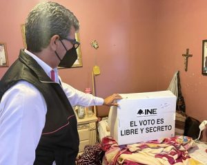Hombre sosteniendo urna de votación para una persona postrada en su cama