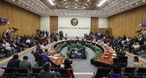 Salón de sesiones con el escudo de México al fondo con letras de color dorado que dice “Instituto Federal Electoral”, mesa en forma de herradura con Consejeros Electorales y representantes de partidos políticos sentados y alrededor de la mesa directores ejecutivos, titulares de unidades técnicas y asesores.