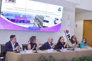 Personas participantes sentados en el estrado frente al público asistente.