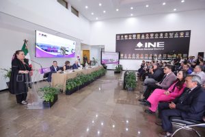 Personas participantes sentados en el estrado frente al público asistente.