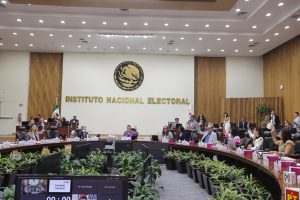 Salón de sesiones con el escudo de México al fondo con letras de color dorado que dice “Instituto Federal Electoral”, mesa en forma de herradura con Consejeros Electorales y representantes de partidos políticos sentados y alrededor de la mesa directores ejecutivos, titulares de unidades técnicas y asesores.