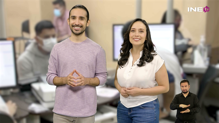 Mujer y hombre de pie sonriendo al frente con un módulo de atención ciudadana al fondo