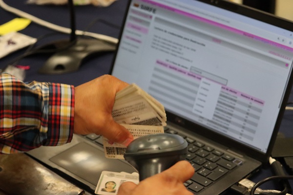 aparece unas manos sosteniendo credenciales para votar y un escaner para su verificación