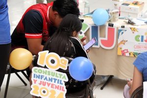 Una menor sentada auxiliada por un adulto en la Consulta Infantil y Juvenil 2024