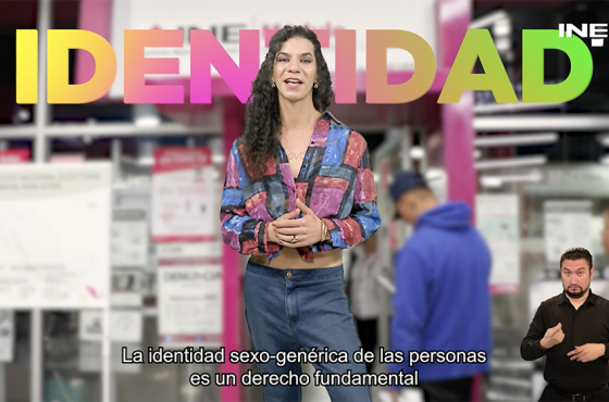Persona Trans de pie con un letrero a sus espaldas que dice "Identidad" con un módulo de atención ciudadana al fondo