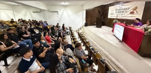 Salón con personas sentadas escuchando la presentación de dos funcionarias del INE en Sonora