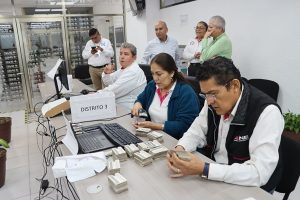 trabajadores del ine sentados en una mesa verificando las credenciales para votar