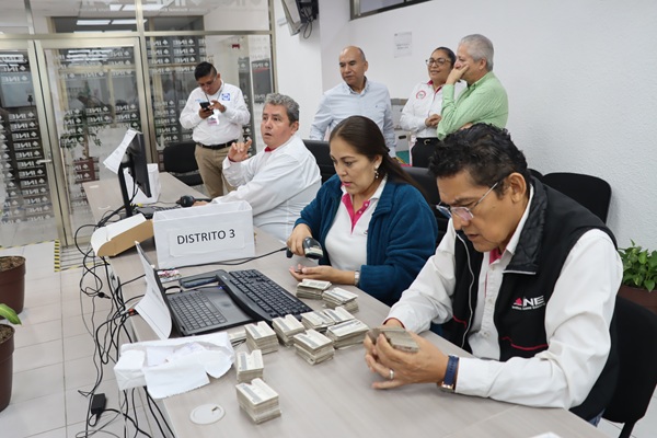 trabajadores del ine sentados en una mesa verificando las credenciales para votar