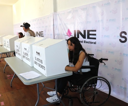 Mujer en silla de ruedas realizando su voto en mampara con la leyenda el voto es secreto