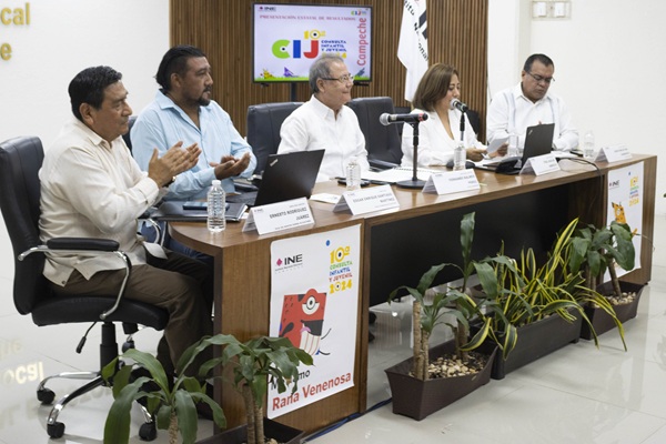 personas sentadas frente a una mesa con un micrófono y una computadora