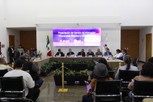 Imagen abierta en el lobby del instituto con las personas participantes sentados en el estrado al frente de la audiencia y letrero del evento.