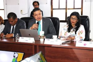 tres personas sentadas, un hombre hablando con micrófono en mano