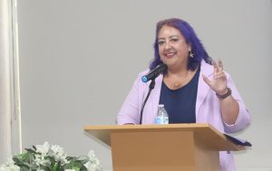 mujer cabello morado de pie frente a un atril con micrófono