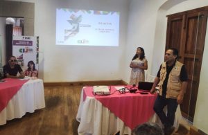 dos personas de pie frente a cuatro personas sentadas