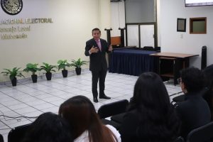 hombre de pie hablando con micrófono frente a estudiantes