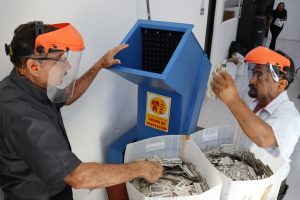 dos hombres con caretas a un costado de una trituradora