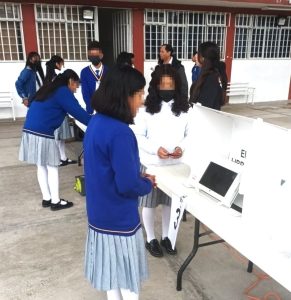 adolescentes mujeres con uniforme azul usando una maquina para votar