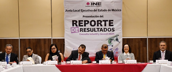 personas en un auditorio sentados frente a una lona con letras negras