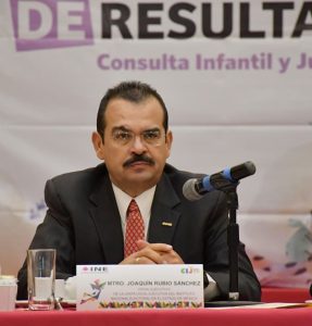 hombre de bigote con lentes sentado frente a un micrófono