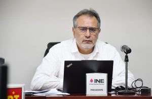 hombre camisa blanca y lentes sentado frente a un micrófono