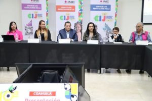 mujeres, hombres y un niño sentados frente a una mesa con micrófonos