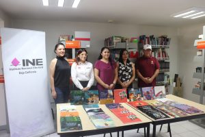 personas de pie frente a una mesa con cinco filas de libros del INE