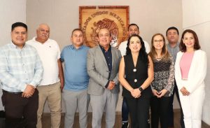 personas de pie frente a un escudo nacional de madera