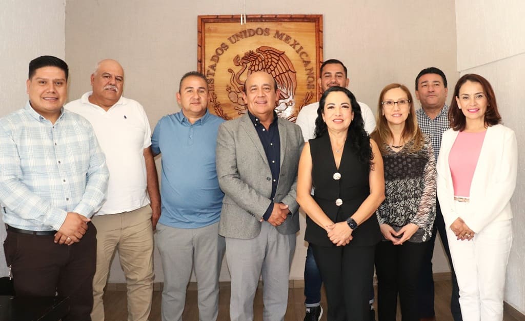 personas de pie frente a un escudo nacional de madera