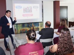 un hombre de pie frente a una pantalla hablando