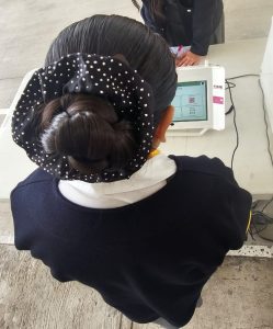 estudiante de espaldas con moño en su cabeza, emitiendo su voto