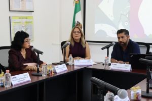 tres personas sentadas frente a una mesa con micrófono
