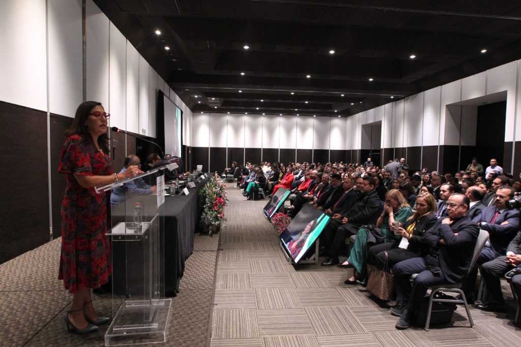 Persona participantes sentadas en el salón enfrente del público asistente en el evento.