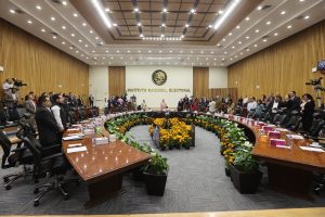 Salón de sesiones con las personas Consejeras Electorales y representantes de partidos políticos parados.