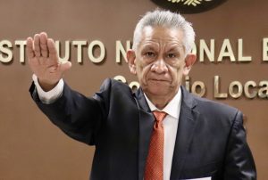 hombre cabello blanco con la mano derecha levantada hacia el frente