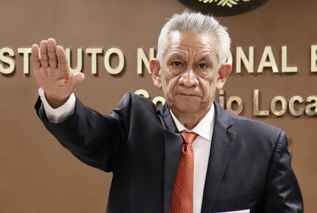 hombre cabello blanco con la mano derecha levantada hacia el frente