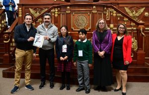 una niña. un niño, dos mujeres, y dos hombres de pie sosteniendo un documento