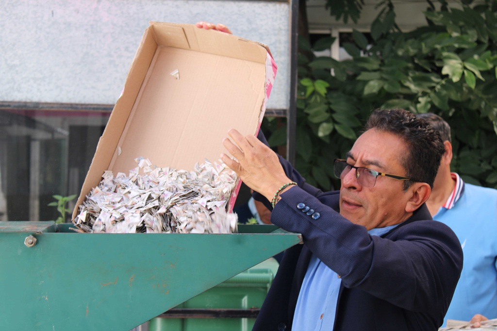 hombre de pie vaciando en una maquina trituradora credenciales para votar