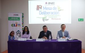 una mujer y dos hombres sentados atrás de una mesa con mantel morado