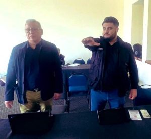 dos hombre de pie, uno de ellos, con el brazo derecho levantado al frente