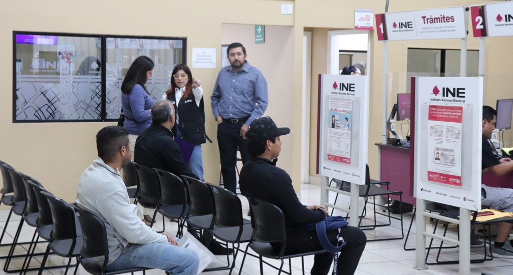 personas sentadas y de pie al interior de un módulo del INE