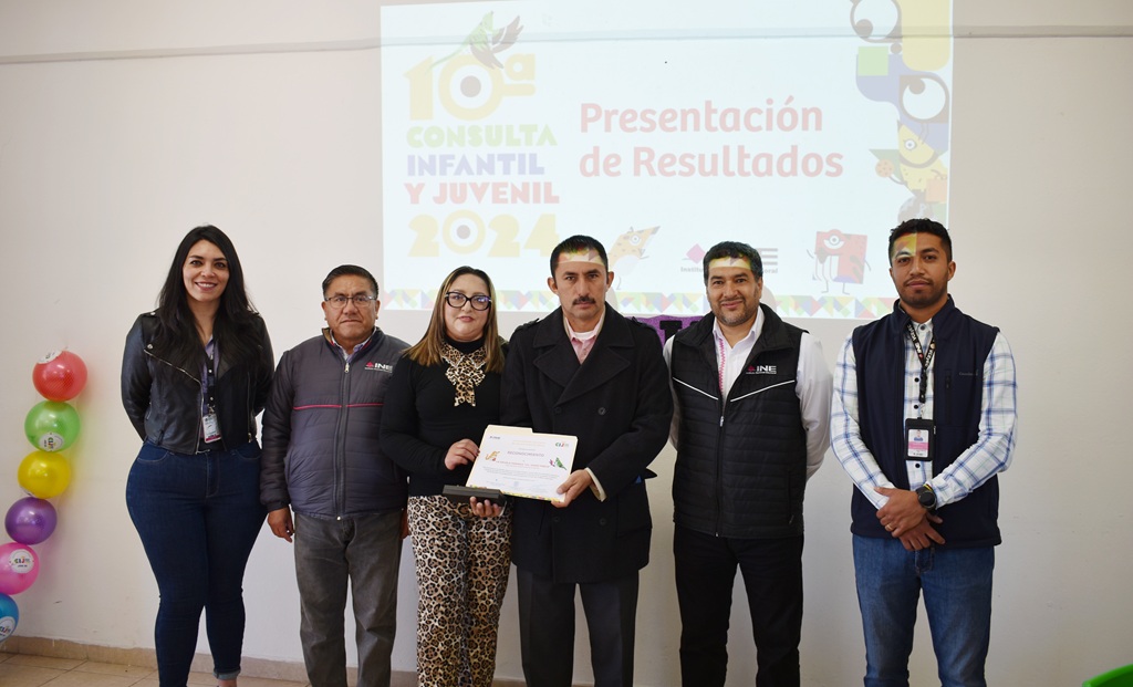 dos mujeres y cuatro hombres de pie sosteniendo un reconocimiento