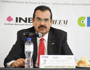 Hombre de lentes y bigote sentado frente a un micrófono