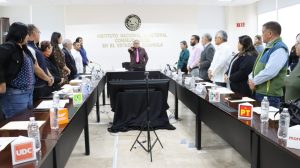personas de pie, un hombre al centro con el brazo derecho al frente