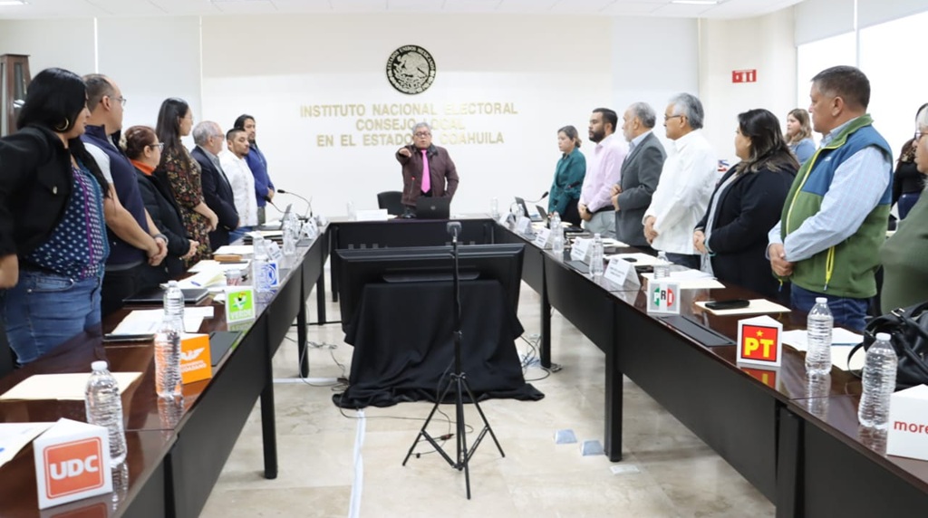 personas de pie, un hombre al centro con el brazo derecho al frente