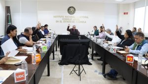 personas sentadas alrededor de una mesa votando a mano alzada.