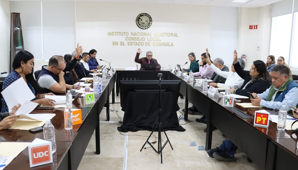 personas sentadas alrededor de una mesa votando a mano alzada.