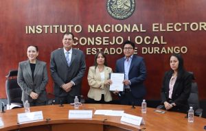 cinco personas de pie, dos de ellos sostienen un documento