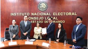 seis personas de pie, dos de ellos al centro sosteniendo un documento