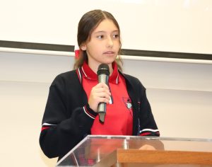 mujer joven con uniforme rojo y azul hablando a treves de un micrófono